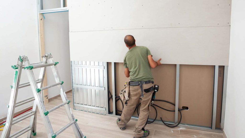 Worker building plasterboard wall. Working with cutting tools, fixing and measuring for drywall.