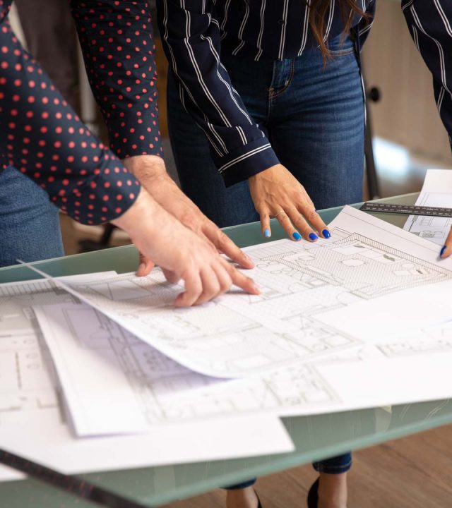 Close up of two architects hands pointing at some drawings. Young person and new ideas